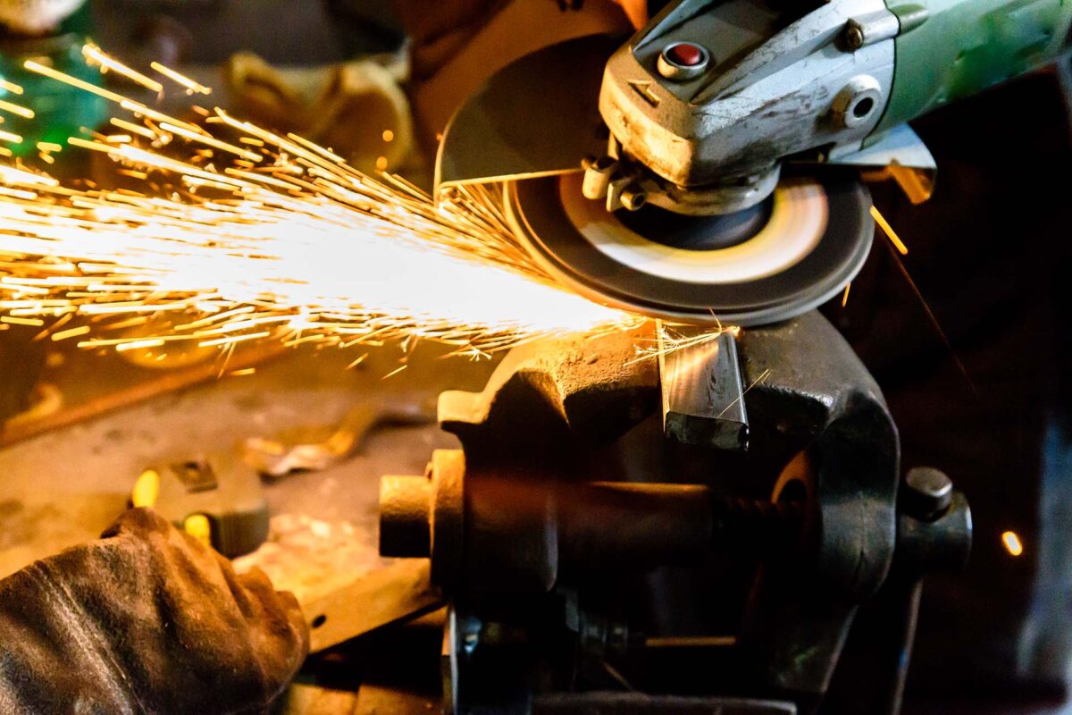 Arbeiter schleift Metallstück und erzeugt leuchtende Funken Funkenflug beim Schleifen von Metall